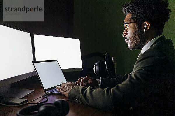 Geschäftsmann mit Mikrofon nutzt Laptop  während er im Heimbüro arbeitet