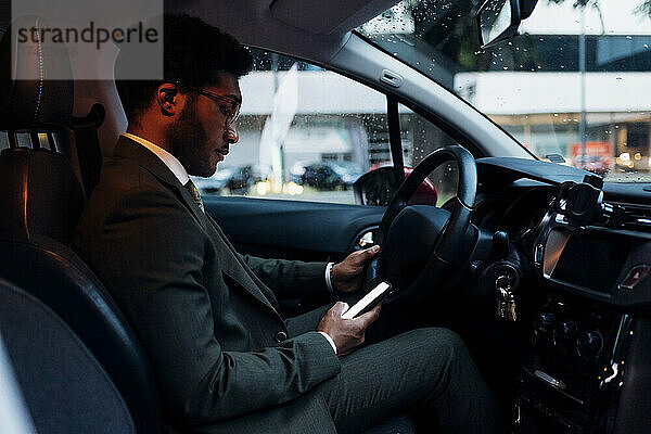 Junger Geschäftsmann benutzt Mobiltelefon  während er im Auto sitzt