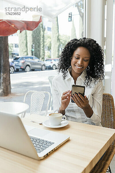 Lächelnde Freiberuflerin benutzt Mobiltelefon  während sie im Café sitzt