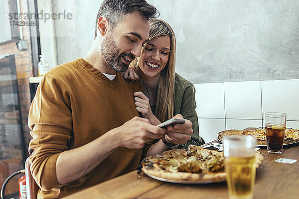 Bärtiger Mann teilt Mobiltelefon mit Freundin am Tisch