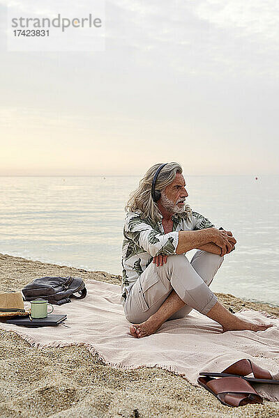 Mann umarmt Knie  während er am Strand Musik hört