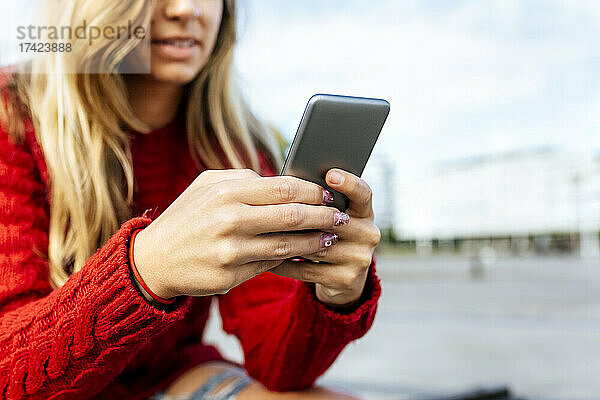 Frau benutzt Smartphone  während sie auf Fußweg sitzt