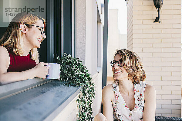 Lächelnde Geschäftsfrau hält Kaffeetasse in der Hand  während sie ihre Kollegin ansieht