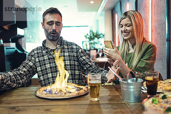 Glückliche Frau fotografiert Pizza von einem männlichen Freund  der im Restaurant schreit