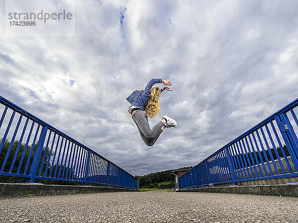 Junge Frau springt gegen bewölkten Himmel über die Remsbrücke
