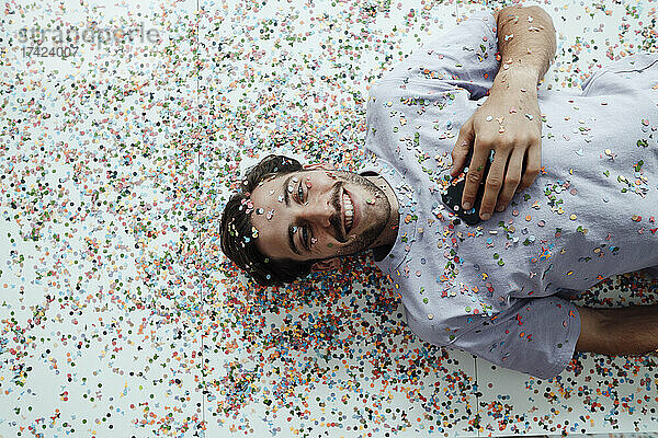 Lächelnder Mann liegt mit Konfetti auf dem Boden
