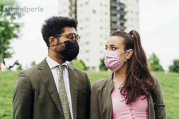 Geschäftspaar mit schützenden Gesichtsmasken  das einander anschaut