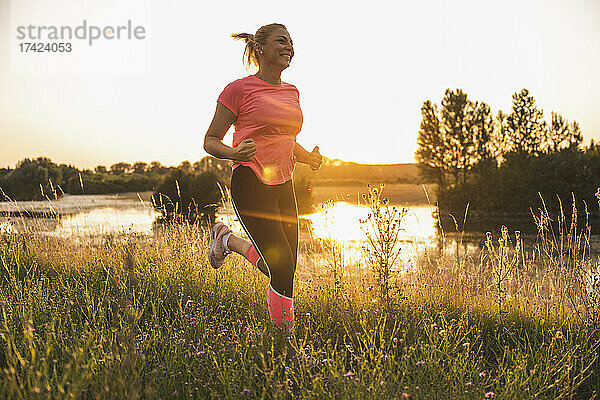 Lächelnde Frau joggt bei Sonnenuntergang auf der Wiese