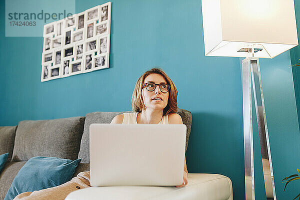 Geschäftsfrau blickt auf beleuchtete Stehlampe  während sie auf dem Sofa sitzt