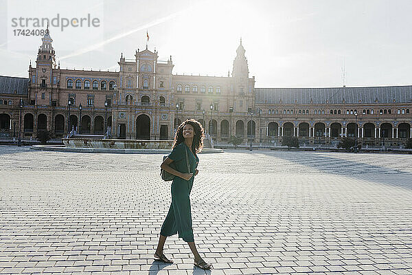 Lächelnde junge Frau  die beim Spaziergang auf der Plaza De Espana in Sevilla  Spanien  wegschaut