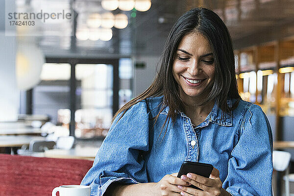 Lächelnde schöne Geschäftsfrau  die Textnachrichten über das Mobiltelefon sendet  während sie im Café sitzt