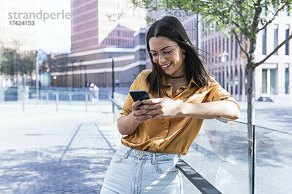 Lächelnde professionelle Textnachrichten per Mobiltelefon  während sie sich an das Geländer lehnt