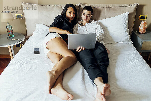 Junge queere Freundinnen benutzen Laptop  während sie zu Hause im Bett liegen