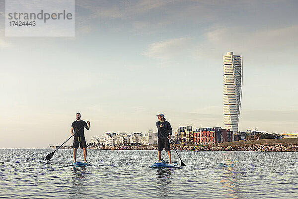 Männliche Freunde Paddleboarding gegen den Himmel im Meer