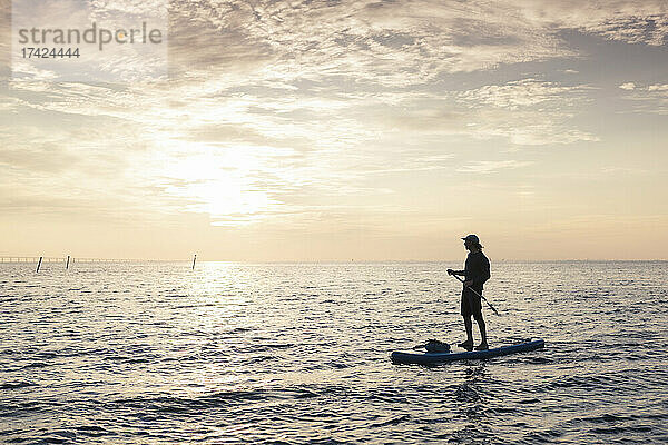 Mittlerer erwachsener Mann schaut weg  während er auf einem Paddleboard im Meer steht