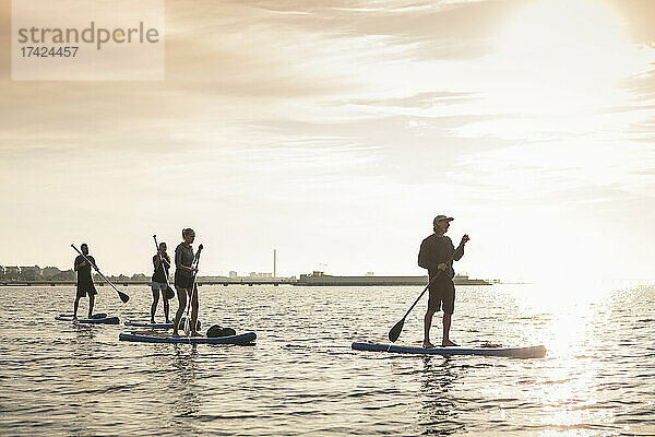 Männliche und weibliche Freunde Paddleboarding im Meer bei Sonnenuntergang