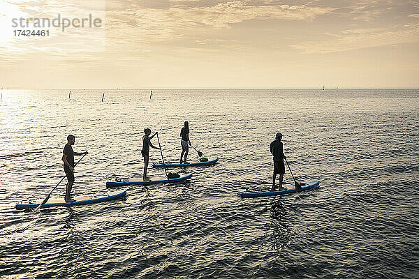 Männer und Frauen paddeln bei Sonnenuntergang auf dem Meer