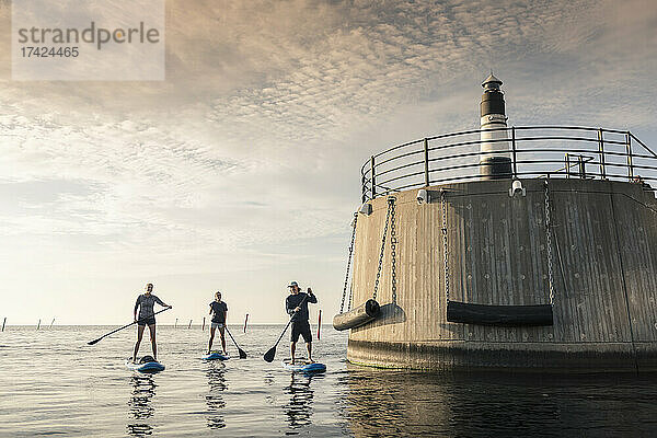 Freundinnen rudern Paddleboard mit männlichem Lehrer am Leuchtturm im Meer