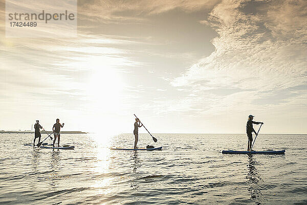 Weibliche und männliche Freunde paddleboarding im Meer während des Sommerurlaubs