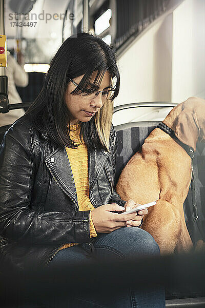 Junge Frau benutzt ein Mobiltelefon  während sie neben ihrem Hund in einer Seilbahn sitzt