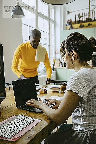 Freiberuflerin arbeitet am Laptop  während der Mann Hausarbeiten erledigt