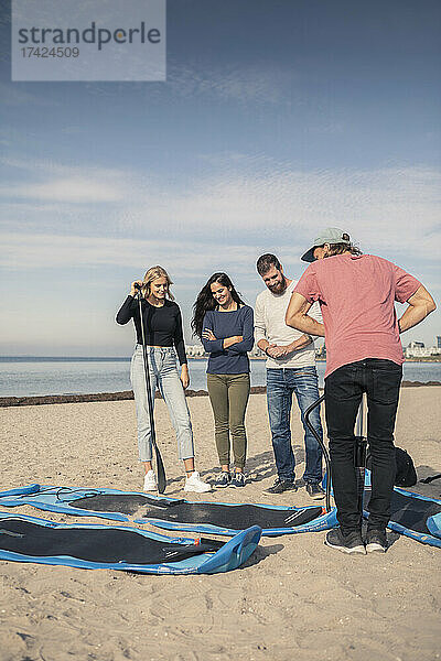 Männlicher Lehrer  der ein Paddleboard aufpumpt  steht bei Freunden am Strand