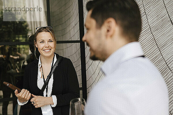 Lächelnde Geschäftsfrau mit Blick auf einen männlichen Unternehmer  der während einer Networking-Veranstaltung im Kongresszentrum diskutiert