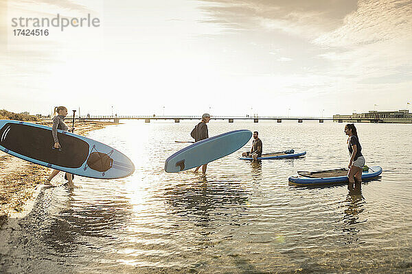 Männliche und weibliche Freunde tragen Paddleboard im Meer