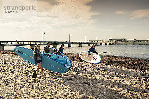 Weibliche und männliche Freunde tragen Paddleboard am Sandstrand