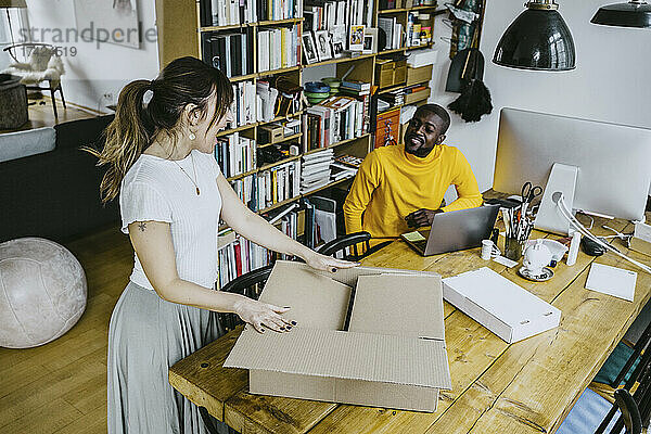 Hohe Winkel Ansicht der männlichen Freiberufler Blick auf glückliche Freundin Öffnung Box stehen am Tisch