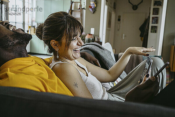 Glückliche Frau und Mann lachen  während sie mit Smartphones auf dem Sofa im Wohnzimmer zu Hause sitzen