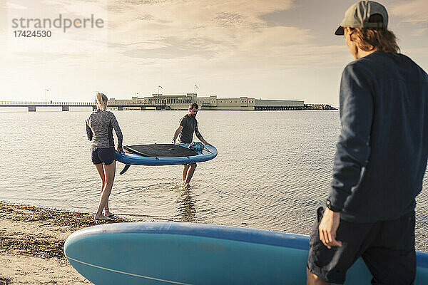 Weibliche und männliche Freunde tragen Paddleboard im Meer am Strand