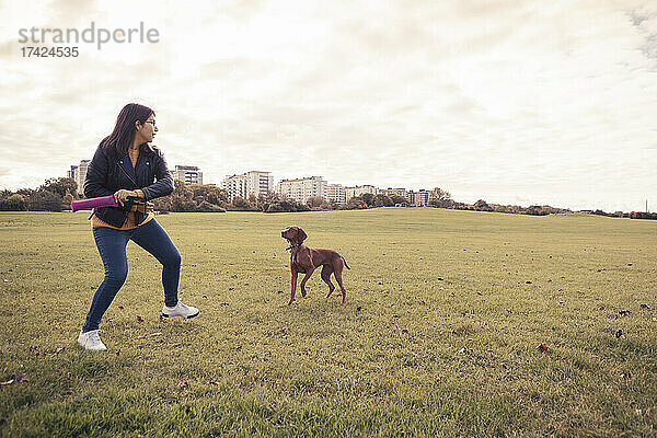 Verspielte junge Frau mit Hund im öffentlichen Park