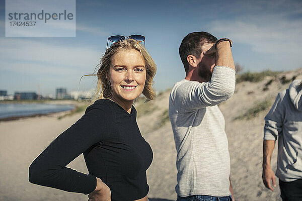 Porträt einer lächelnden Frau mit männlichen Freunden am Strand an einem sonnigen Tag
