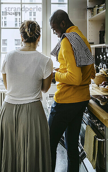 Rückansicht einer mittleren erwachsenen Frau  die mit ihrem Freund in der Küche zu Hause steht