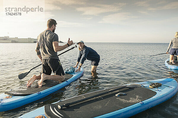 Mann lernt Paddelboard von männlichem Lehrer im Meer am Strand