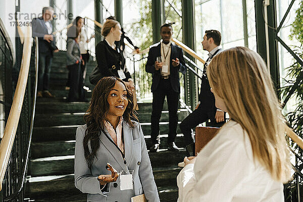 Geschäftsfrau gestikuliert  während sie mit einer weiblichen Fachkraft diskutiert  während sie an einer Treppe im Kongresszentrum steht