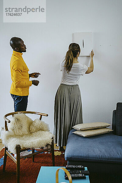 Mid erwachsene Frau hängen Gemälde an der Wand stehend von Mann im Wohnzimmer zu Hause