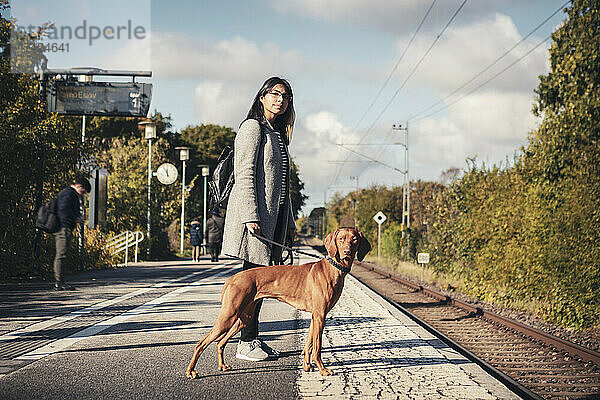 Junge Passagierin und Hund warten am Bahnhof an einem sonnigen Tag