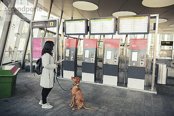 Junge Frau mit Hund am Fahrkartenautomaten im Bahnhof