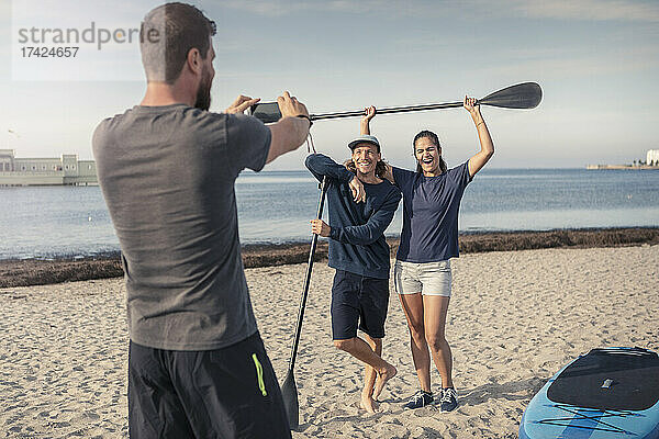 Mann fotografiert glückliche männliche und weibliche Freunde am Strand während des Sommerurlaubs