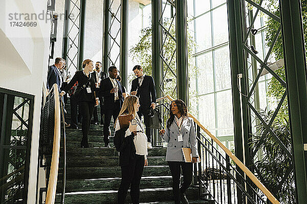 Geschäftsfrau und Geschäftsmann gehen eine Treppe hinunter  während sie im Kongresszentrum miteinander diskutieren
