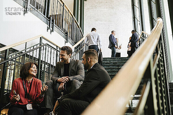 Lächelnde weibliche Fachkraft diskutiert mit männlichen Kollegen auf der Treppe sitzend während eines Seminars