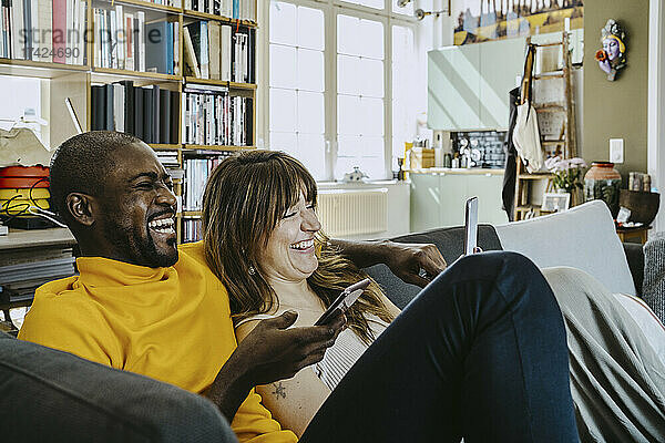 Fröhliches Paar sitzt zusammen mit Handys auf dem Sofa im Wohnzimmer zu Hause
