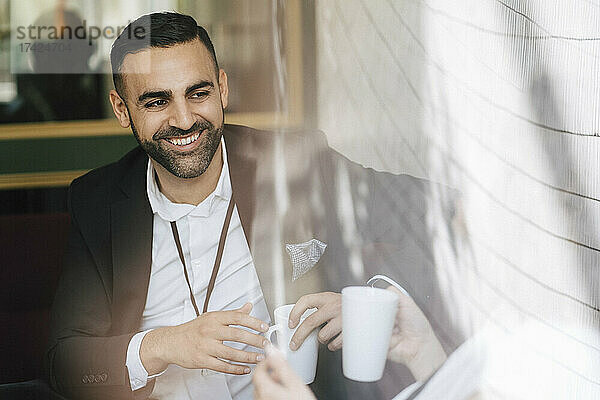Glücklicher männlicher Unternehmer  der mit einer Kaffeetasse dasitzt und eine Kollegin anschaut  die im Kongresszentrum diskutiert