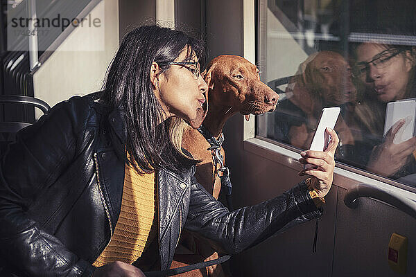 Junge Frau spricht Selfie mit Hund durch Smartphone in Seilbahn