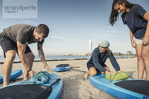 Männliche und weibliche Freunde binden Schlauchboot auf Paddleboard am Strand