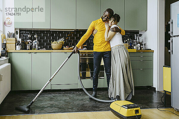 Volle Länge der Mitte erwachsene Frau umarmt Freund mit Staubsauger in der Küche zu Hause