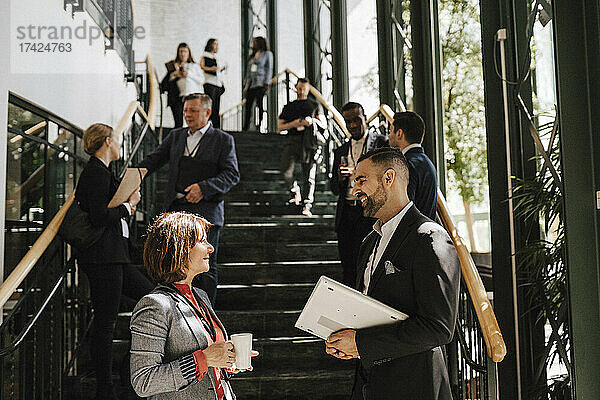 Lächelnder Geschäftsmann  der mit einer reifen Frau diskutiert  während er an einer Treppe im Kongresszentrum steht