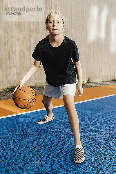 Porträt eines Mädchens  das auf einem Sportplatz Basketball dribbelt
